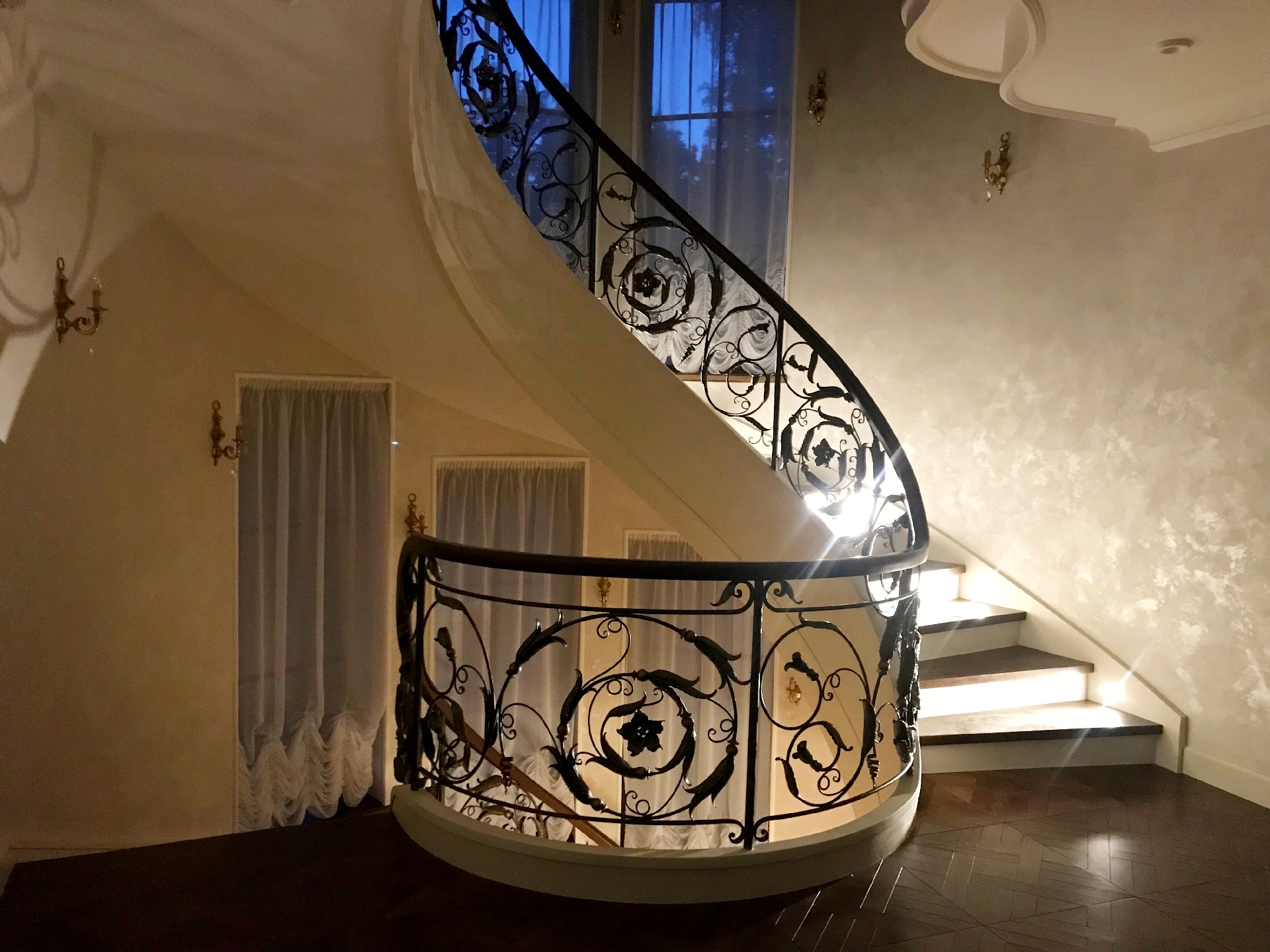 Спиральная лестница с кованым ограждением с яркой боковой подсветкой ступеней